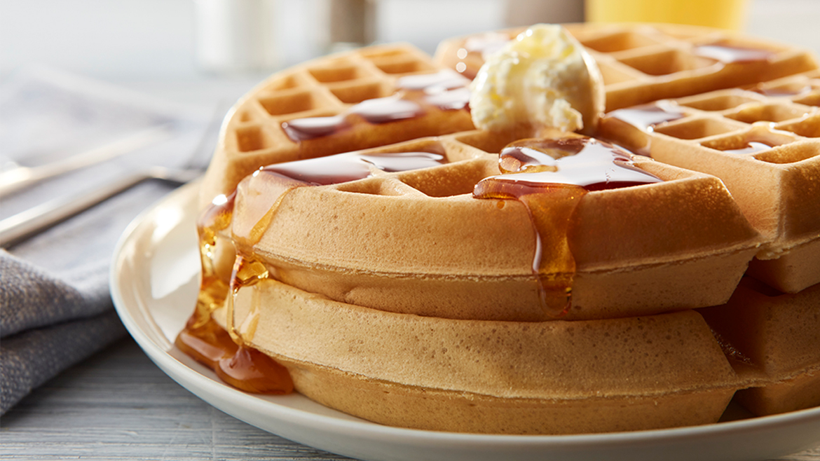 Two round waffles stacked on a plate with butter and syrup