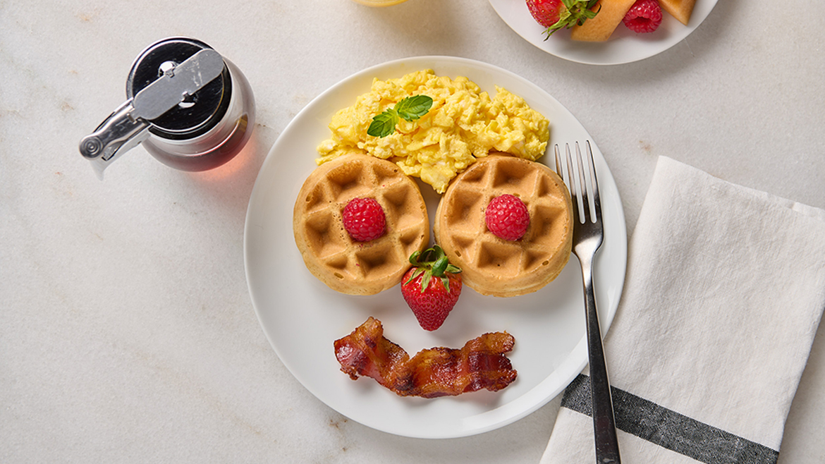 Two waffles, eggs, bacon, and berries arranged in happy face on plate