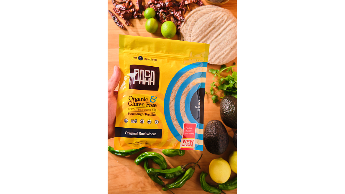 Hand holding Pacha tortillas over table with assorted vegetables