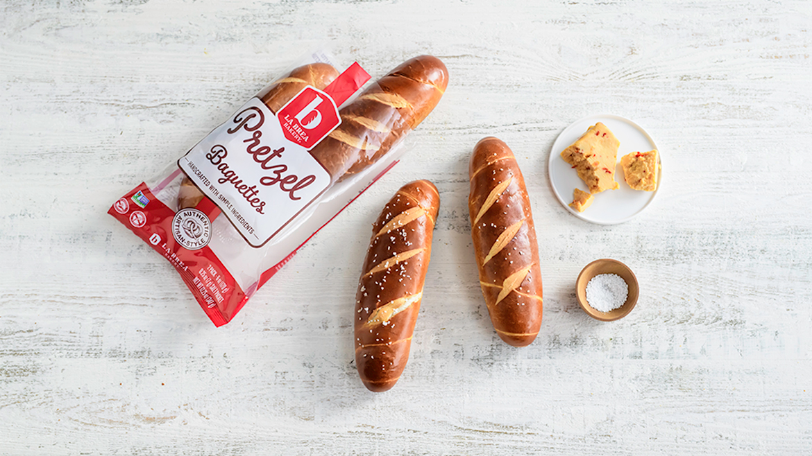 Two loaves of pretzel baguette, with salt in a bowl plus a plate and the package of Pretzel Baguettes to the left.