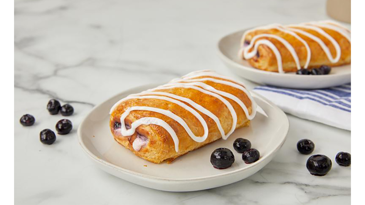 Two blueberry Flips pastries on plates, atop a table