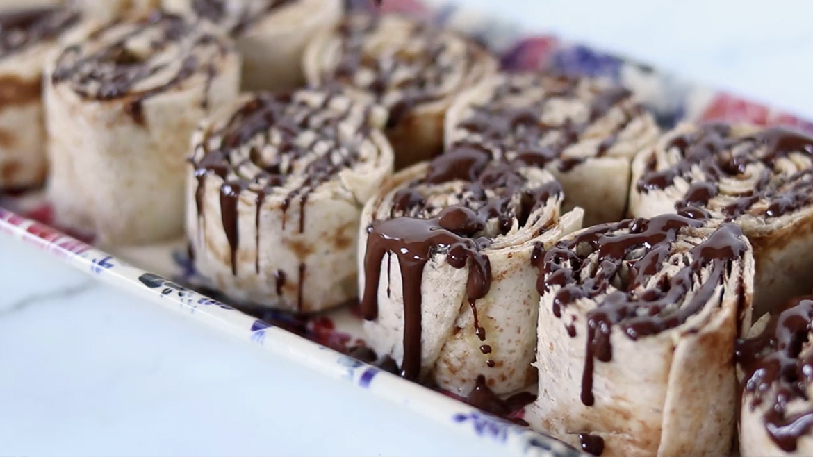 Paper plate on a marble counter with tortilla cinnamon roll desserts drizzled with chocolate
