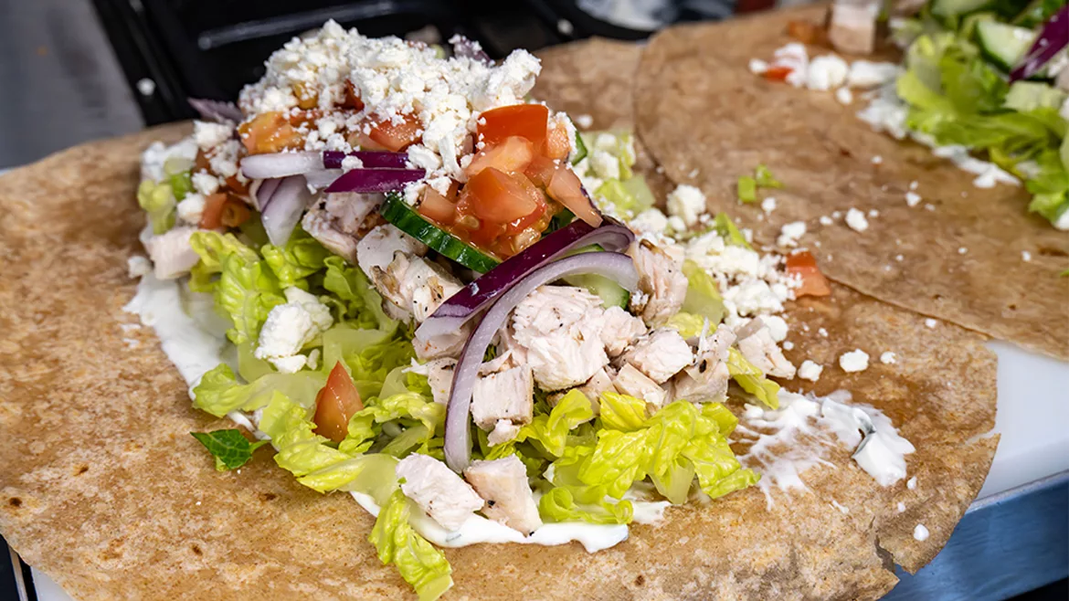 A buffet counter with two open tortillas loaded with Greek chicken toppings