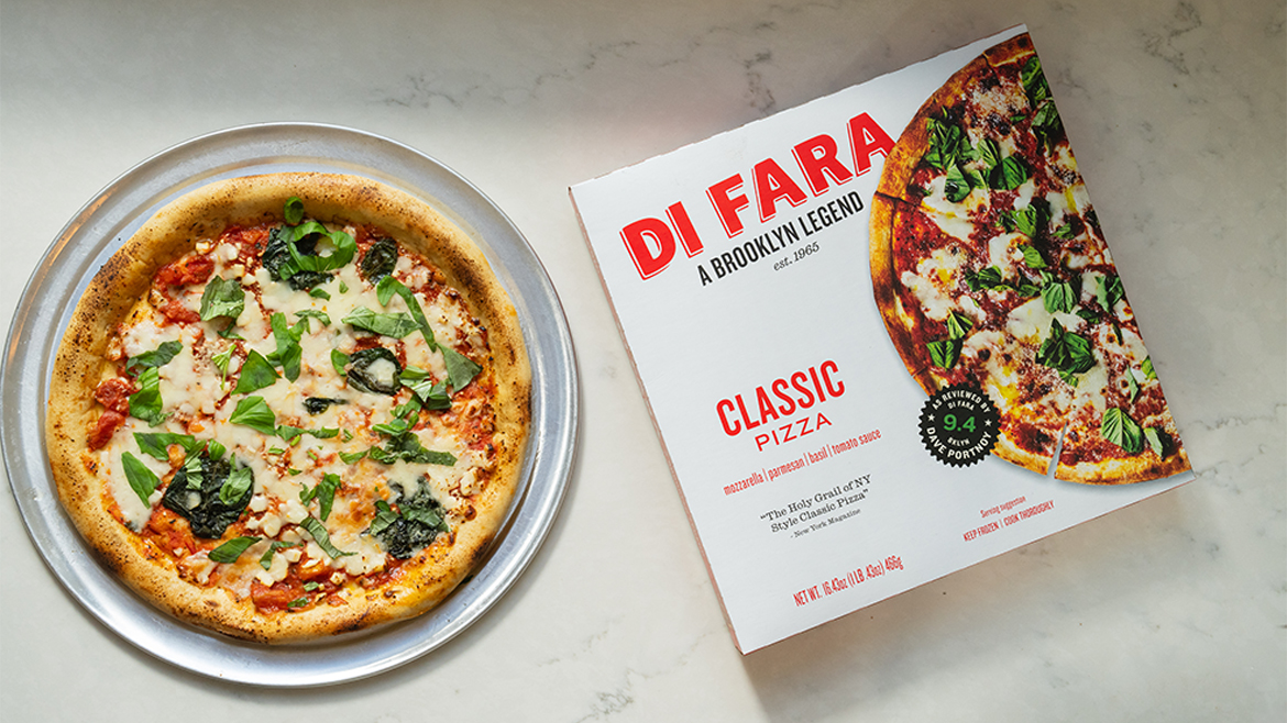A pizza with mozzarella, parmesan, basil, and tomato sauce, on a serving plate, next to a white and red pizza box.