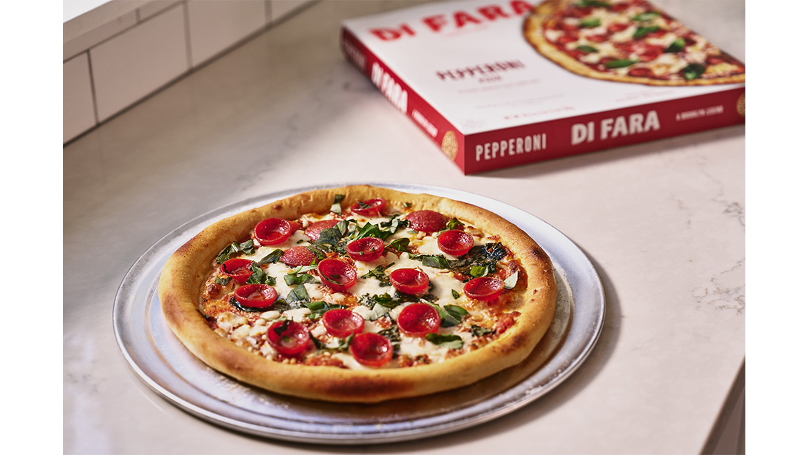A pepperoni pizza on a serving plate, next to a white and red pizza box.