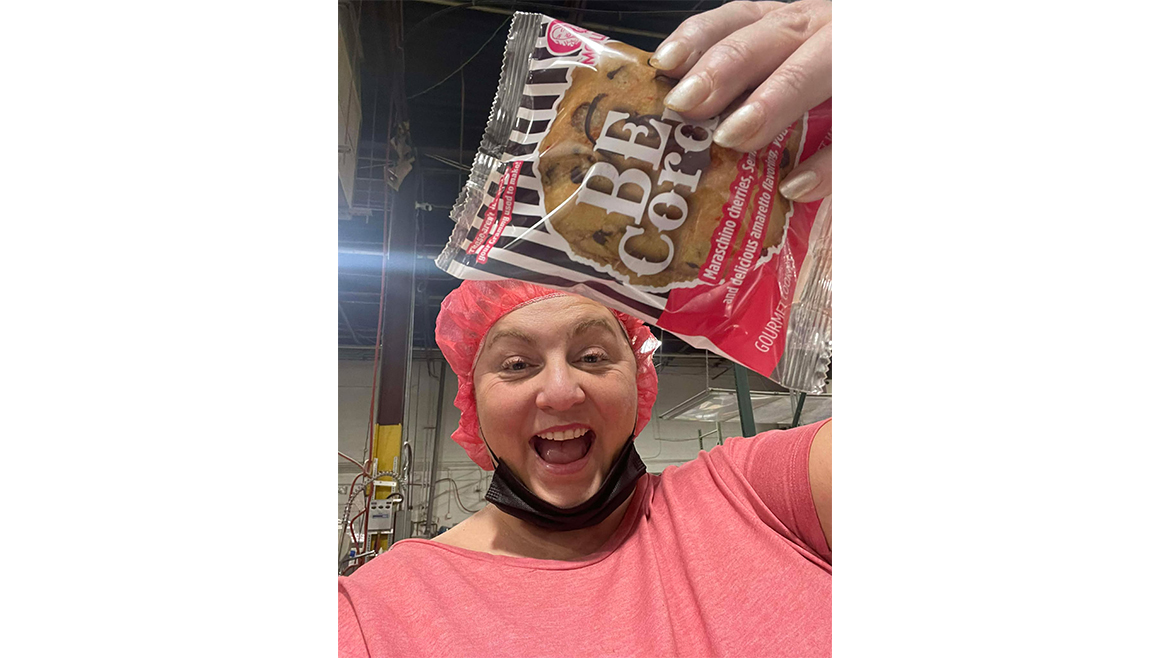 White woman in pink shirt and pink hairnet holding Molly Bz cookie