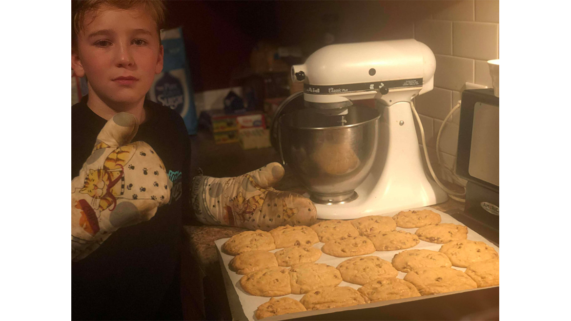 Young boy next to mixer and sheet full of freshly baked cookies