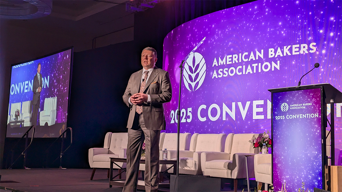 A man in a grey suit speaks, at ABA Convention 2025, on the main stage.