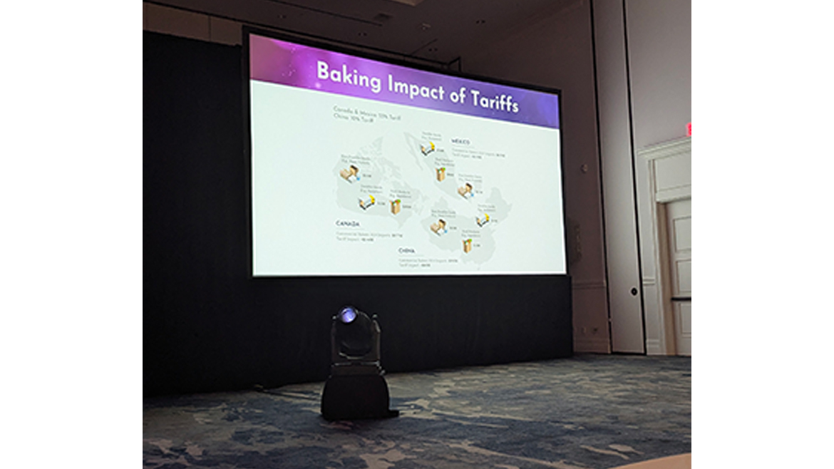 A screen labeled Baking Impact of Tariffs with a table in the foreground and pen and paper, at ABA Convention 2025.