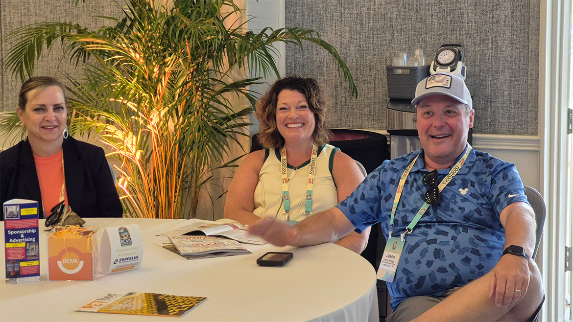 Two women and one man with conference badges and lanyards sitting at a table.