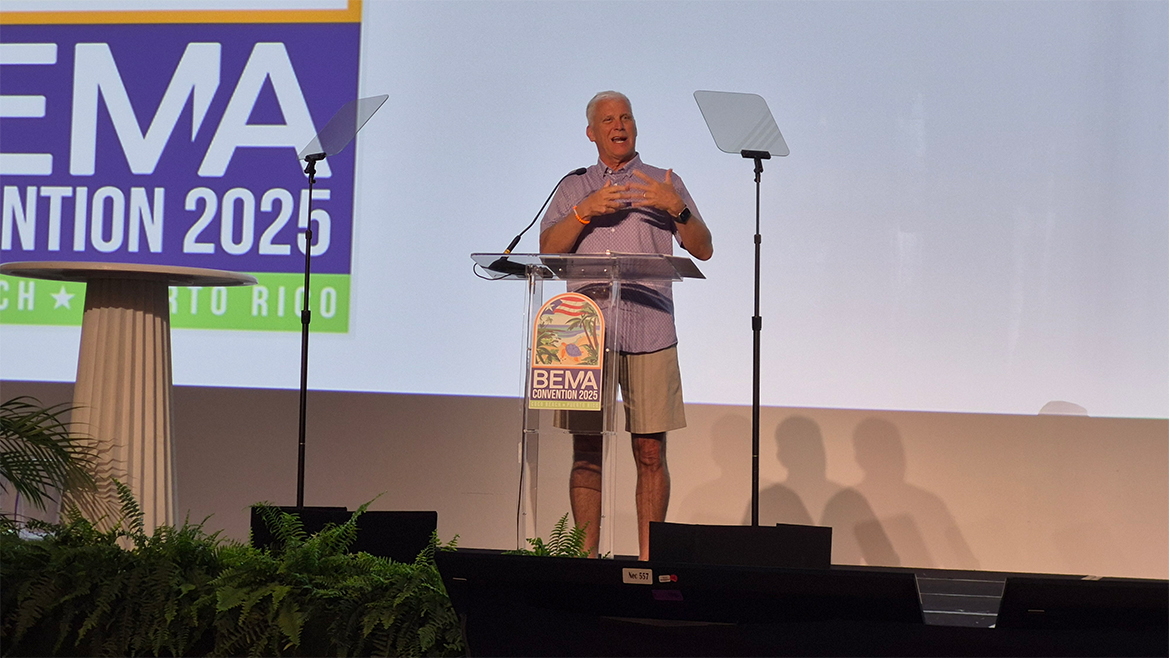 A man wearing a button-down shirt and khaki shorts speaking on a podium.