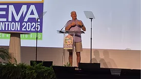 A man wearing a button-down shirt and khaki shorts speaking on a podium.