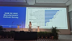 A woman wearing a blazer and a skirt presenting in front of a chart on a screen.