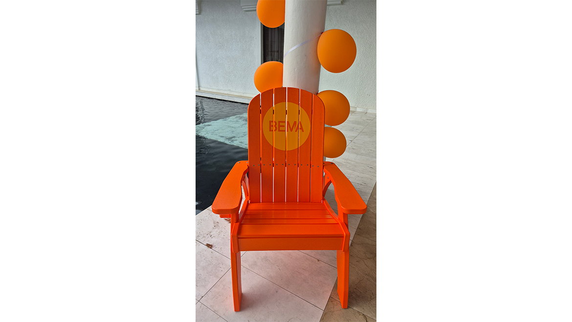 An orange deck chair with BEMA written on it in a yellow circle, plus orange balloons in background.