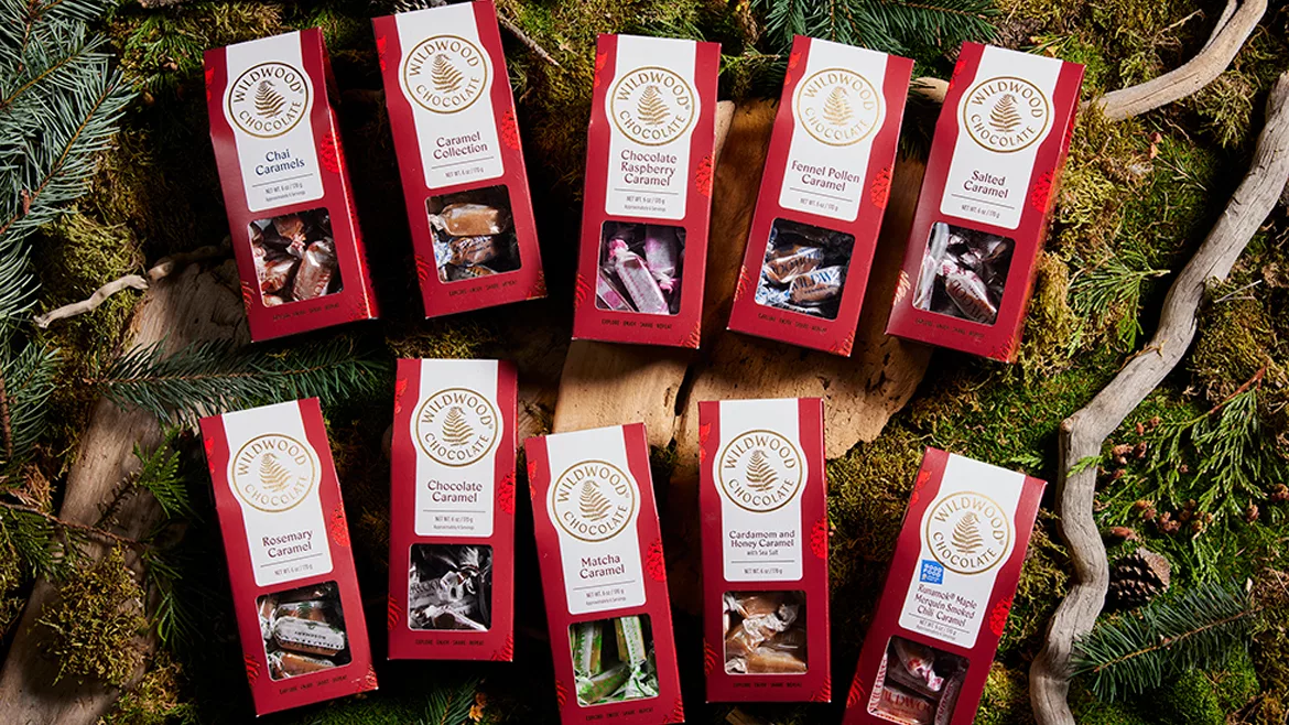 Ten red packages of Wildwood caramels, all different flavors, against a background of twigs and greenery.