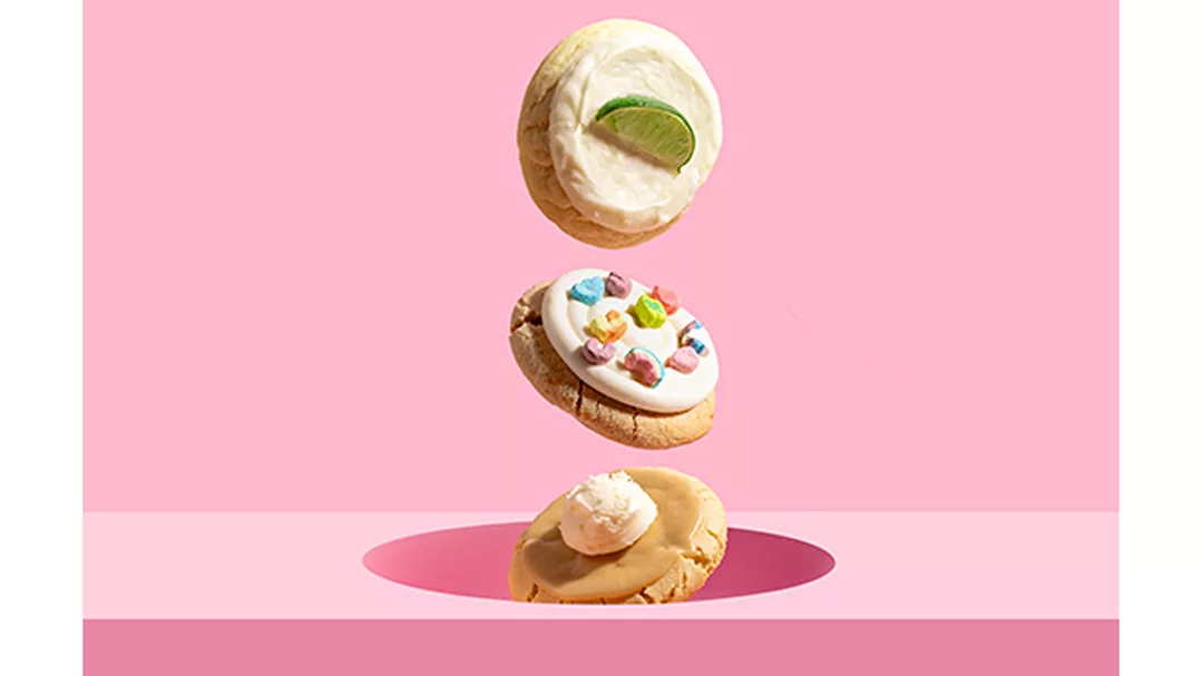 Three gravity-defying Crumbl cookies in front of pink background