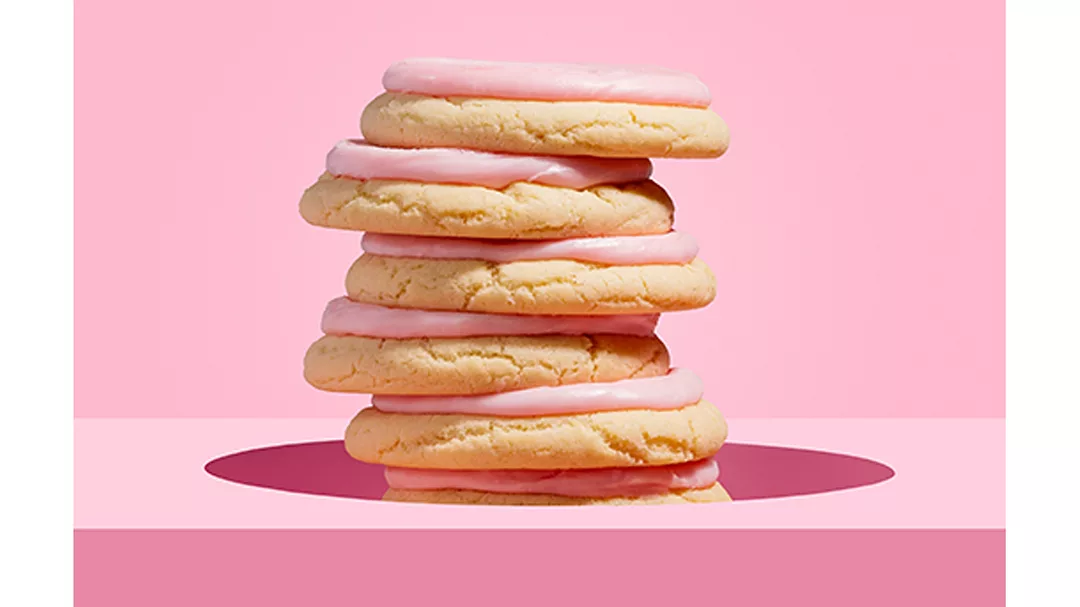Stack of Crumbl pink frosted sugar cookies over pink background