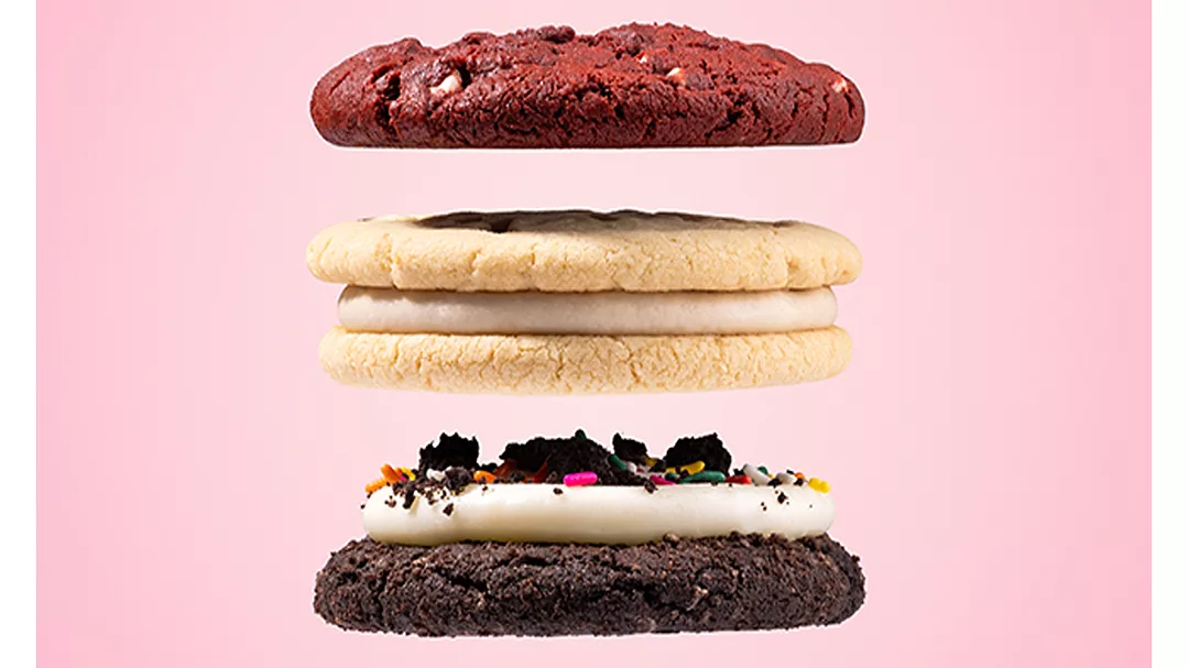Three Crumbl cookies stacked in front of pink background