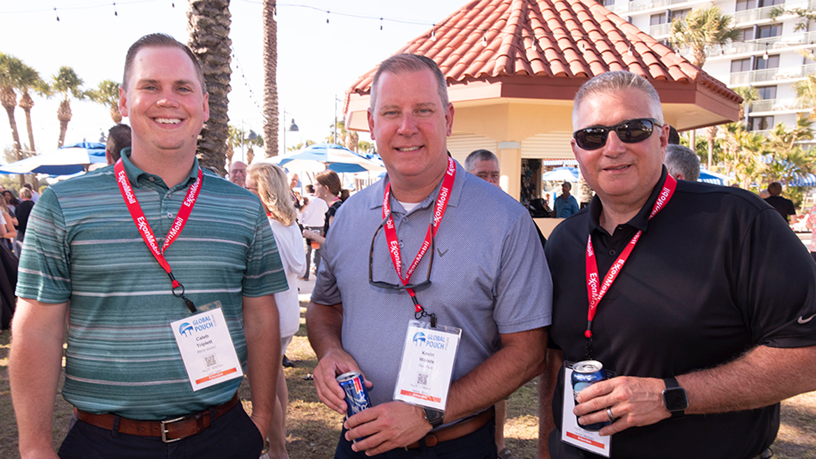 Three men with conference lanyards standing outside and holding beverage cans.