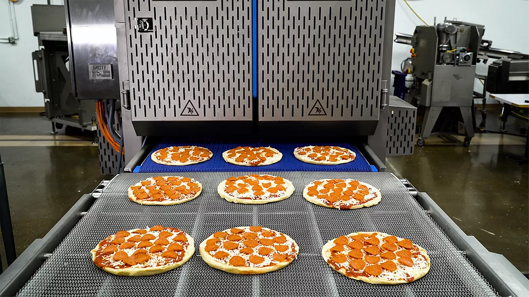 Pepperoni pizzas going down conveyor of Grote slicer