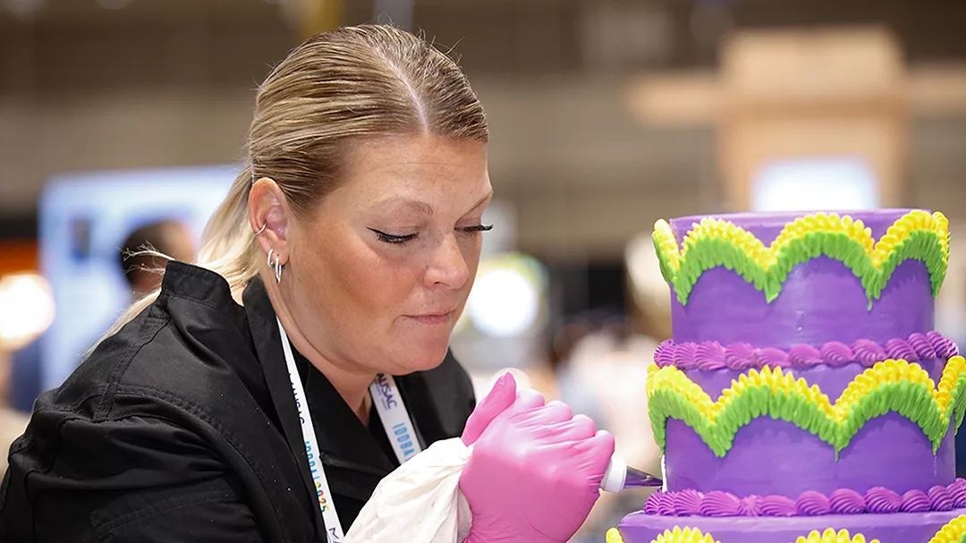 Woman decorating purple and green tiered cake