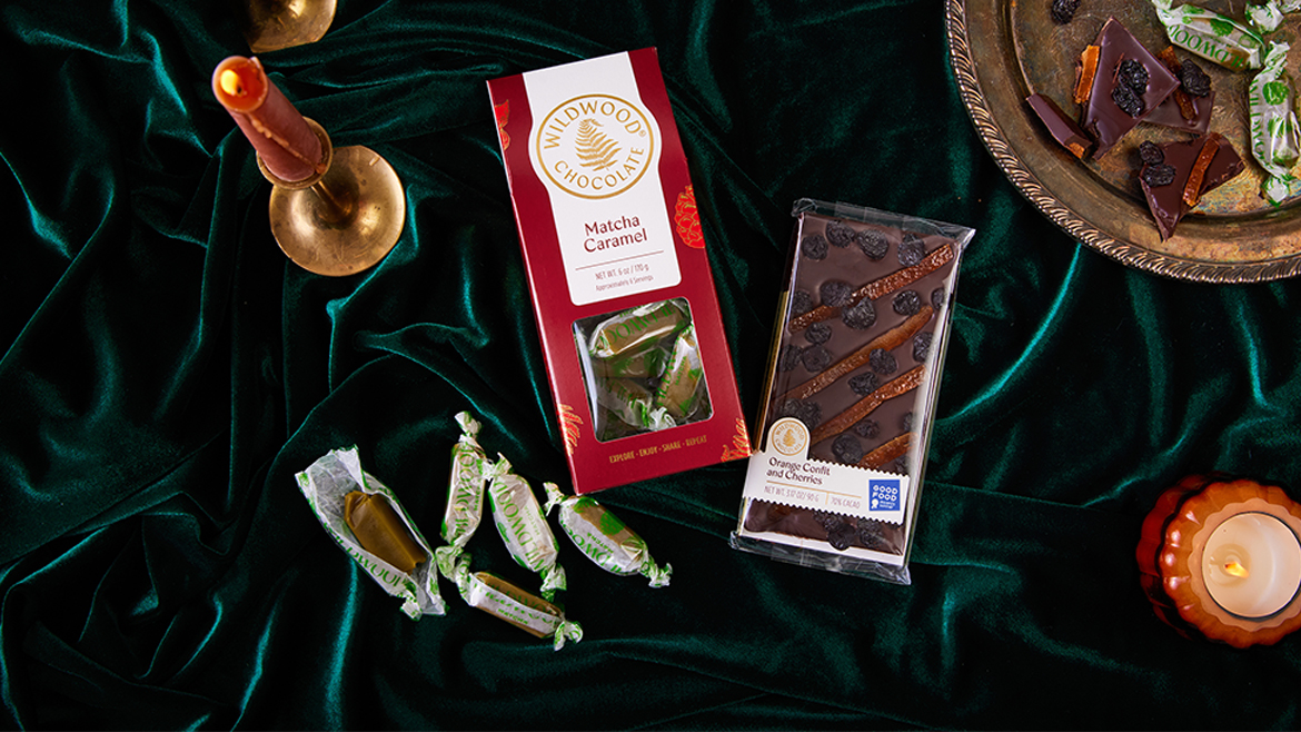 A red package of Wildwood’s Matcha Caramels plus Orange Confit and Cherries, with individually wrapped caramels, on a green velvet blanket.